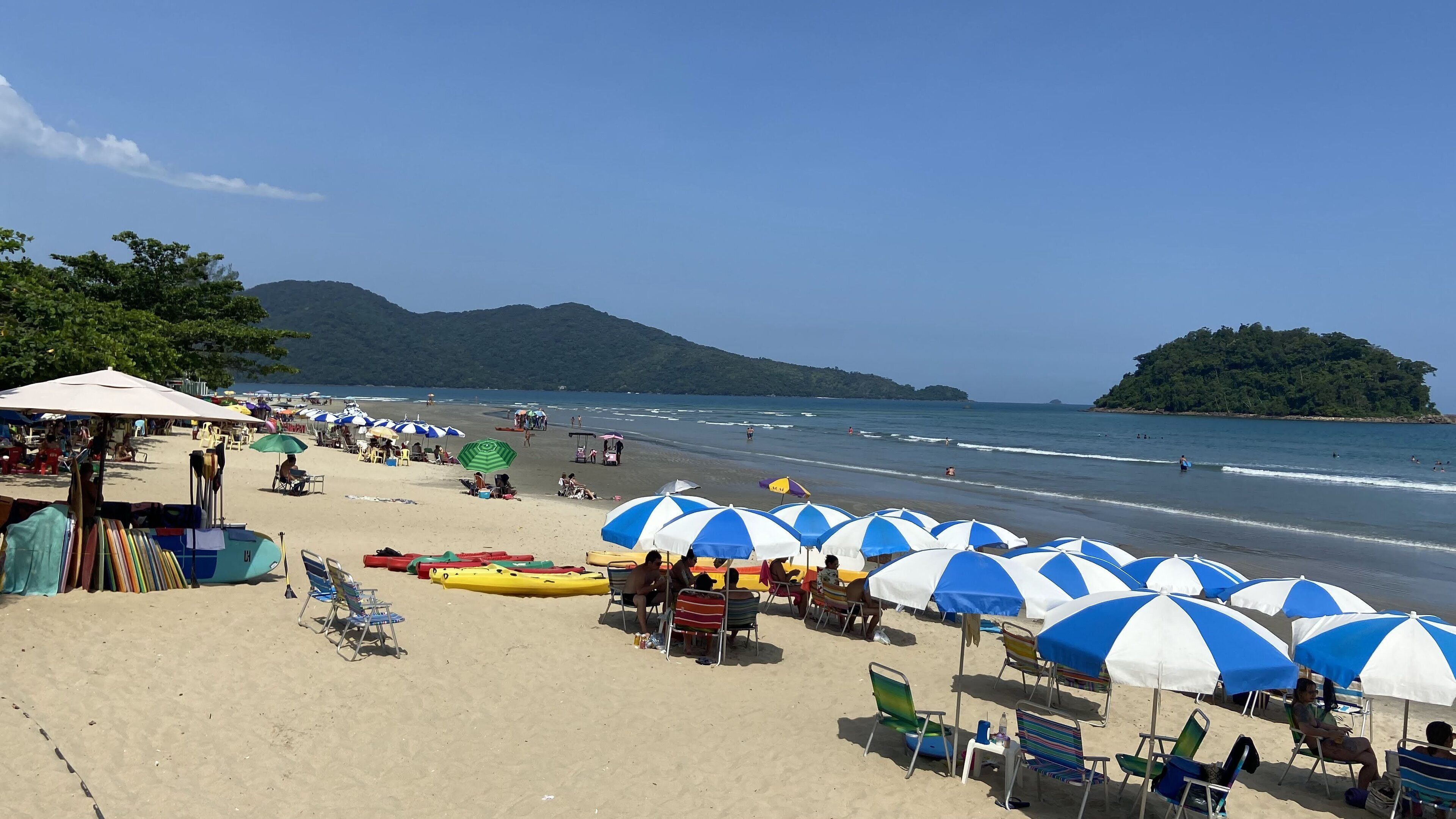 A beach with rows of blue and white umbrellas, beach chairs, and kayaks.
