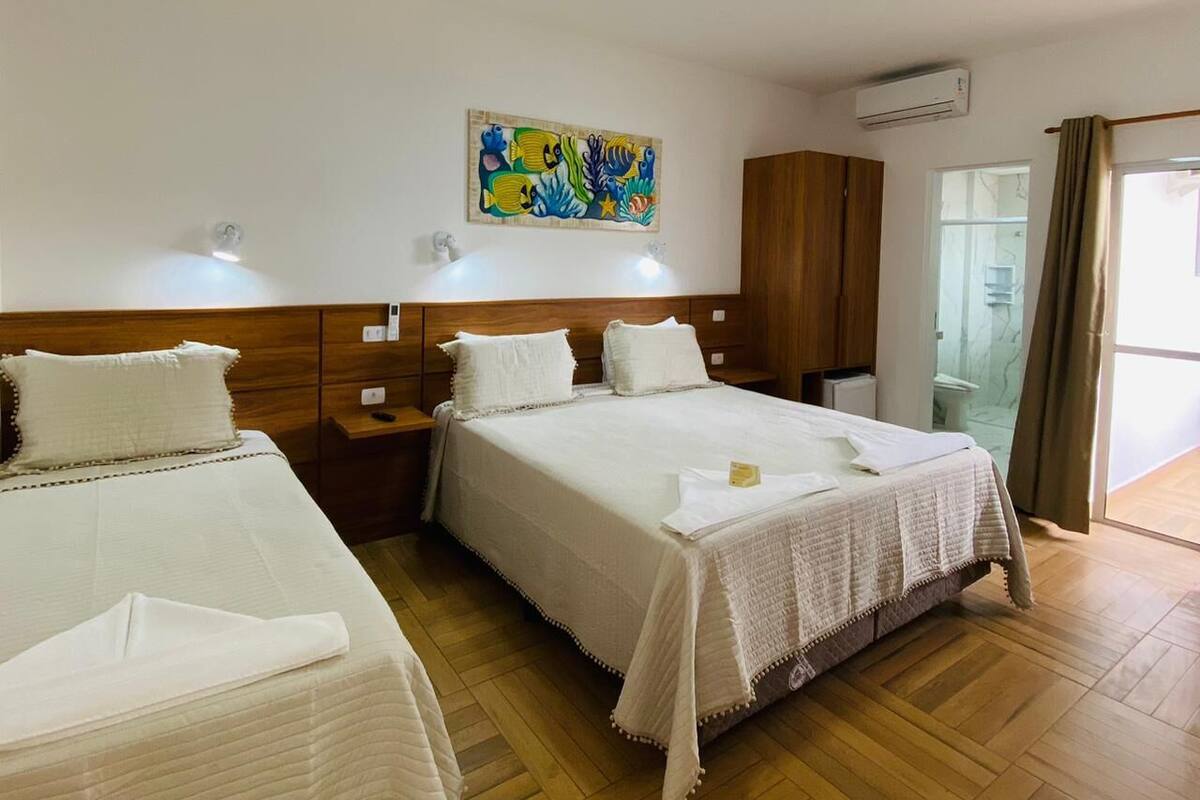 Hotellihuone, jossa on kaksi sänkyä, puinen sängynpääty, taulu seinällä ja kylpyhuone, joka näkyy lasiovesta.