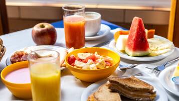 Una tavola da colazione con diversi cibi, tra cui una ciotola di insalata di frutta, un bicchiere di succo d'arancia, una fetta di anguria, un panino con formaggio grigliato e un piatto con uova strapazzate e pane tostato.