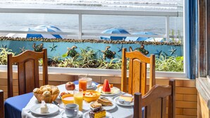 A breakfast table with various foods and drinks, overlooking the ocean with beach umbrellas and sea turtles in the background. - Pousada Kaliman Ubatuba (Ubatuba)