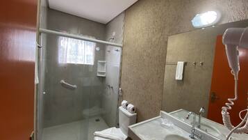A bathroom with a glass shower enclosure, a toilet with toilet paper, a sink with a mirror, and a hairdryer on the wall.