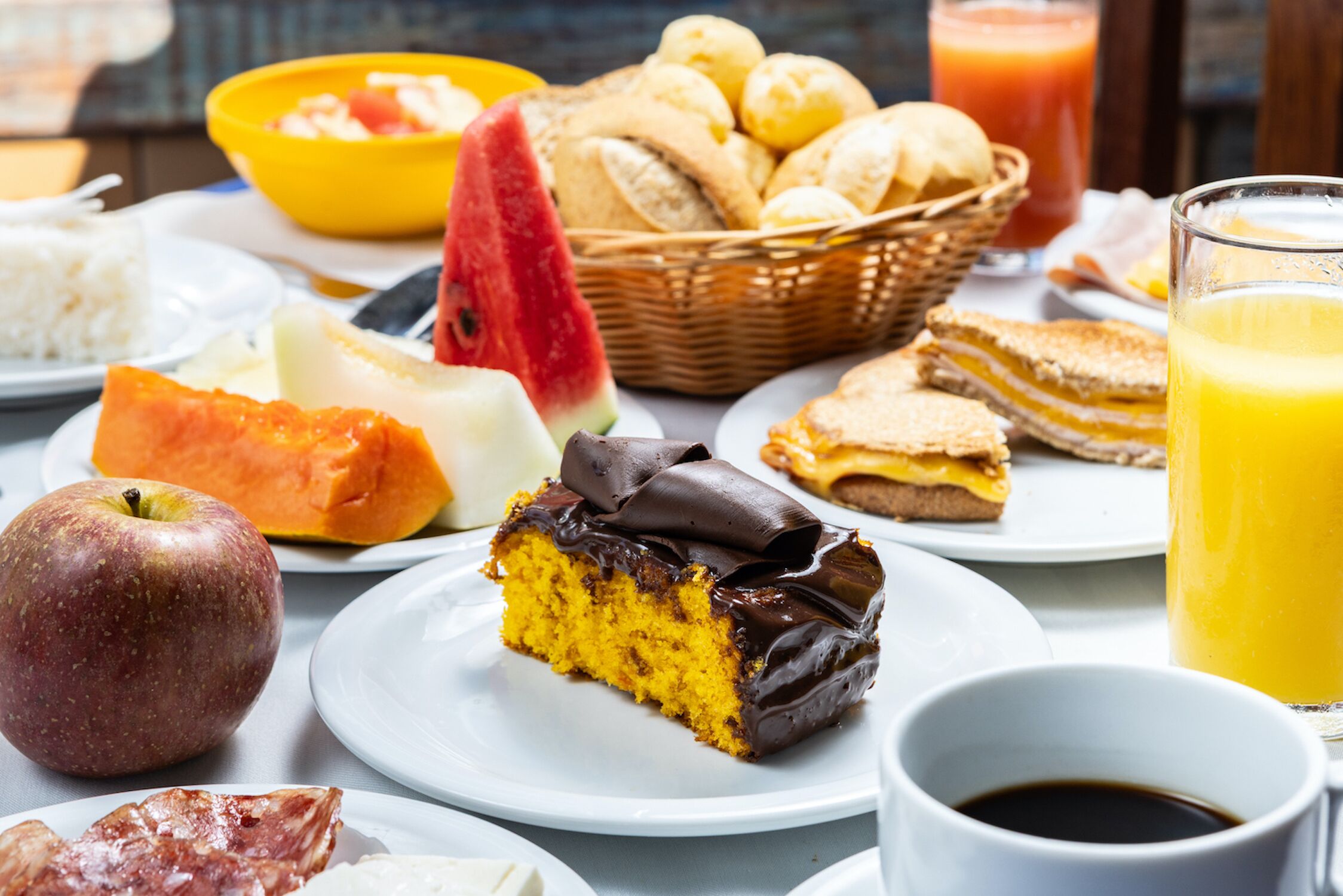 A breakfast setting with various food items including a slice of cake, fruit, bread, and a glass of orange juice.