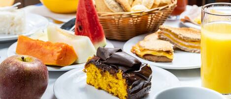 A breakfast setting with various food items including a slice of cake, fruit, bread, and a glass of orange juice.