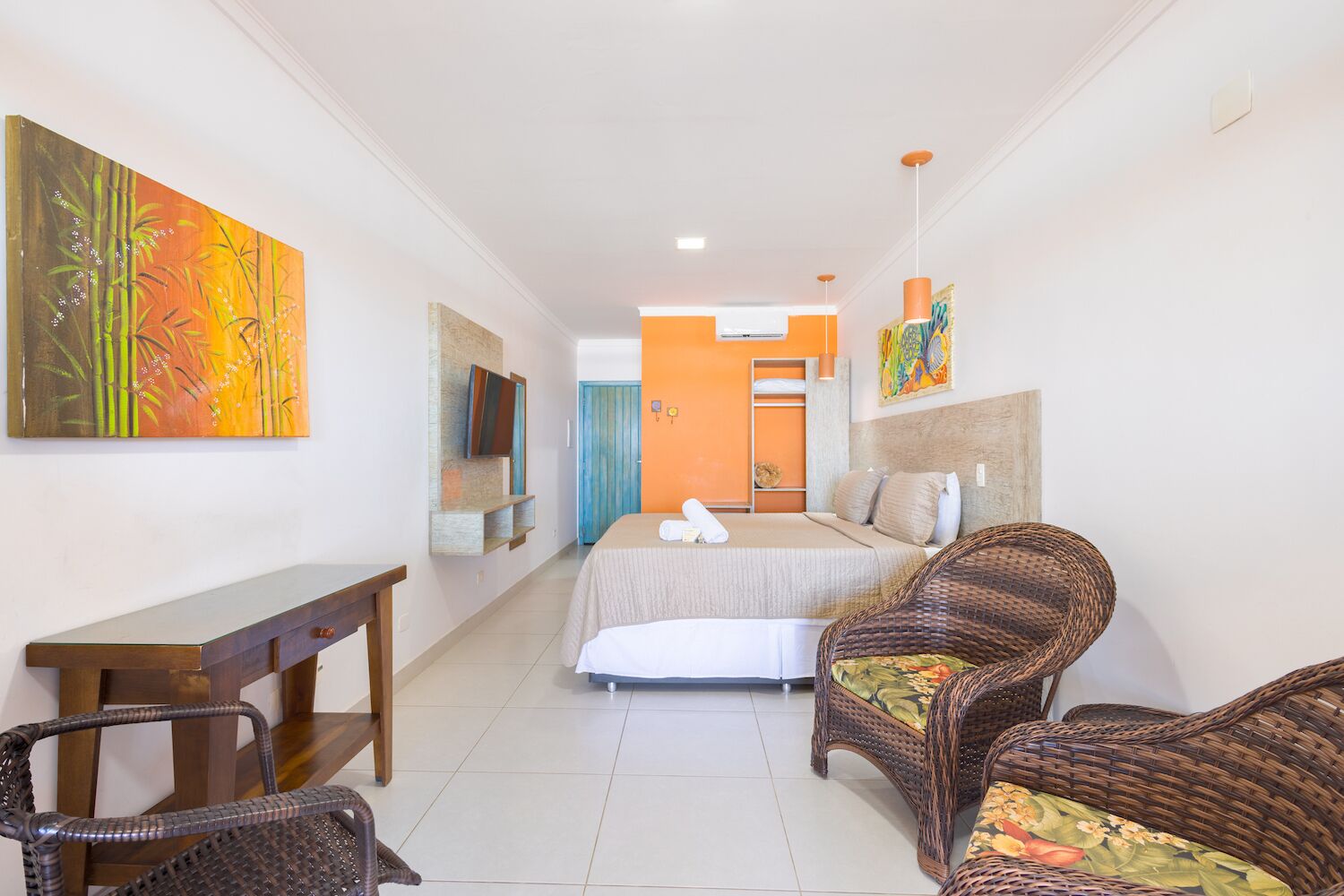 A hotel room with a bed, two wicker chairs, a wooden desk, and a painting on the wall.