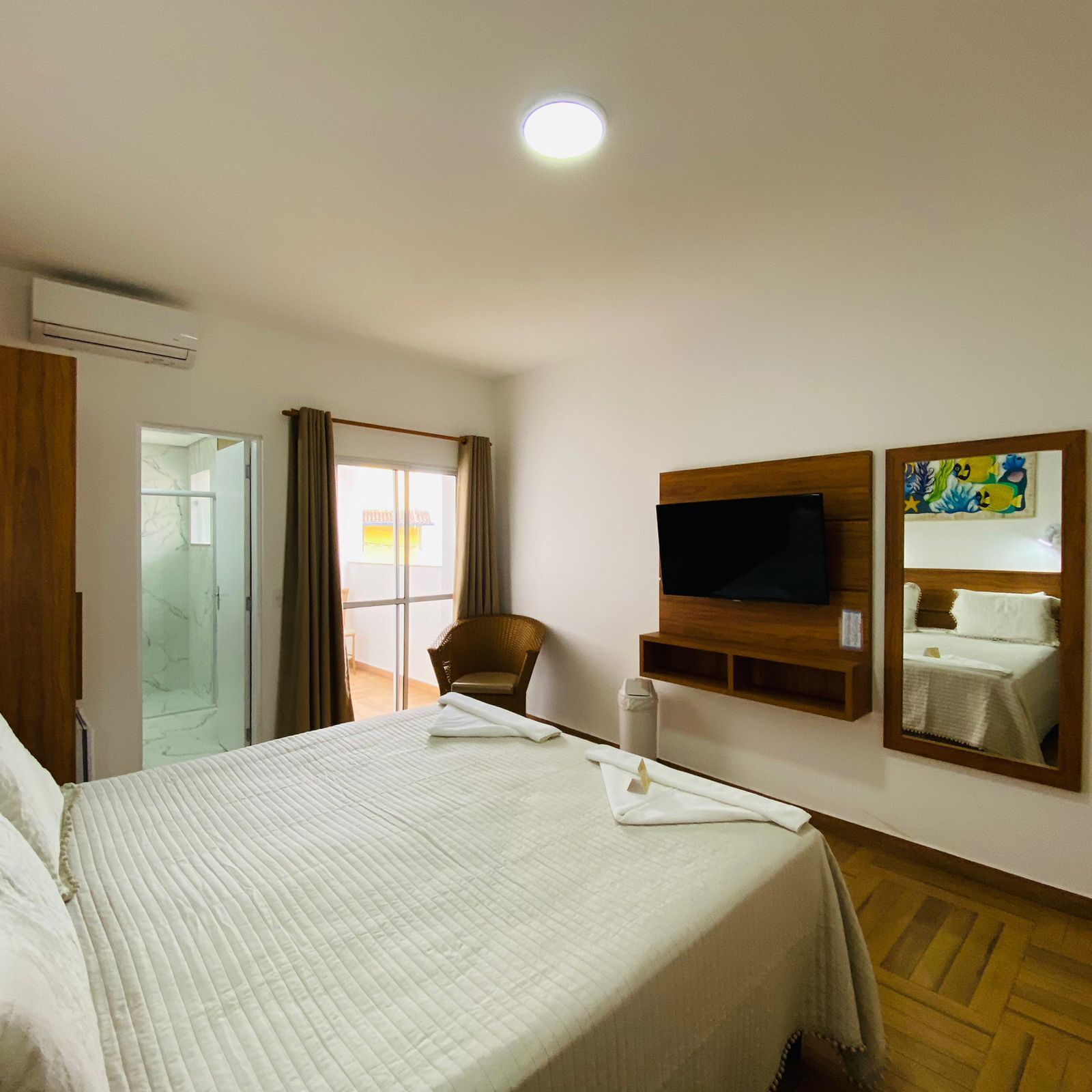 Ein Hotelzimmer mit Bett, Fernseher, Spiegel und einem Fenster mit Vorhängen.