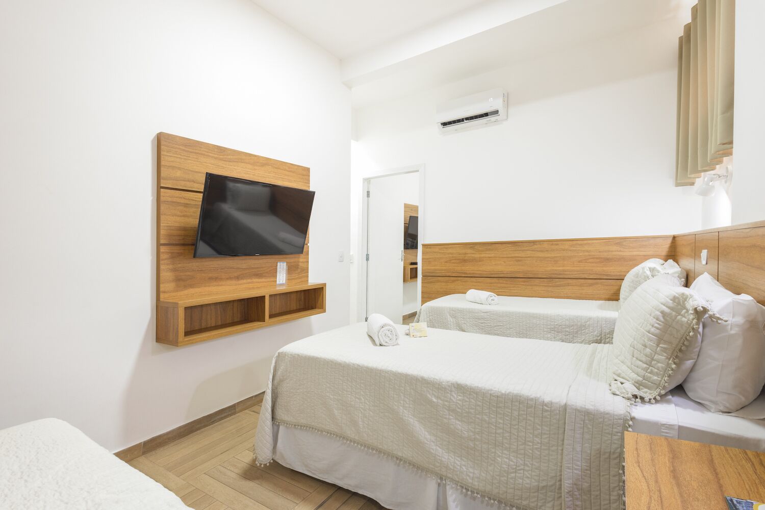 Ein Hotelzimmer mit einem Holz-Kopfteil, einem an einer Holzablage montierten Flachbildfernseher, zwei Betten mit weißer Bettwäsche und einem Holzboden.