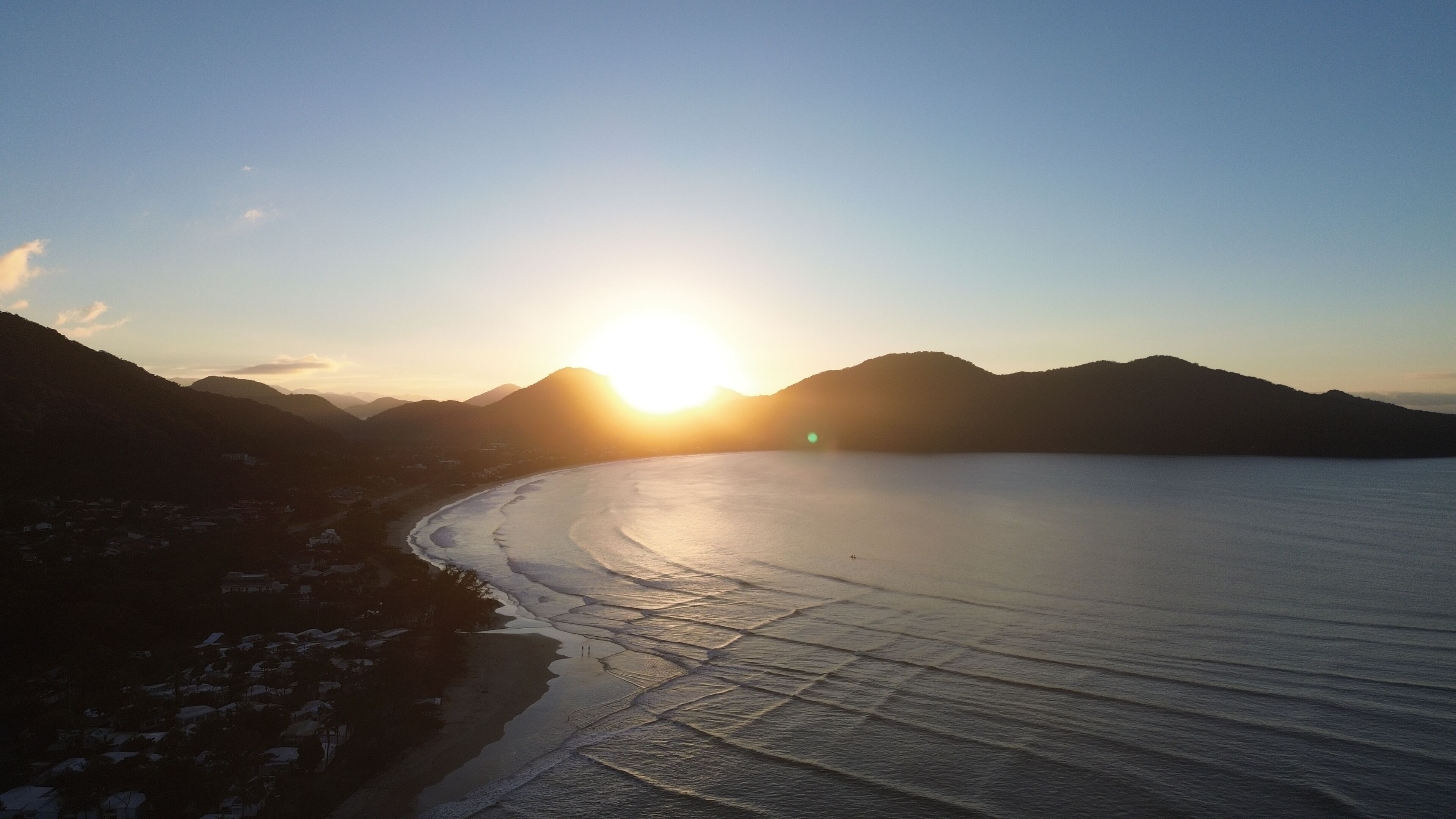 A coastal landscape with a body of water, mountains, and a clear sky.