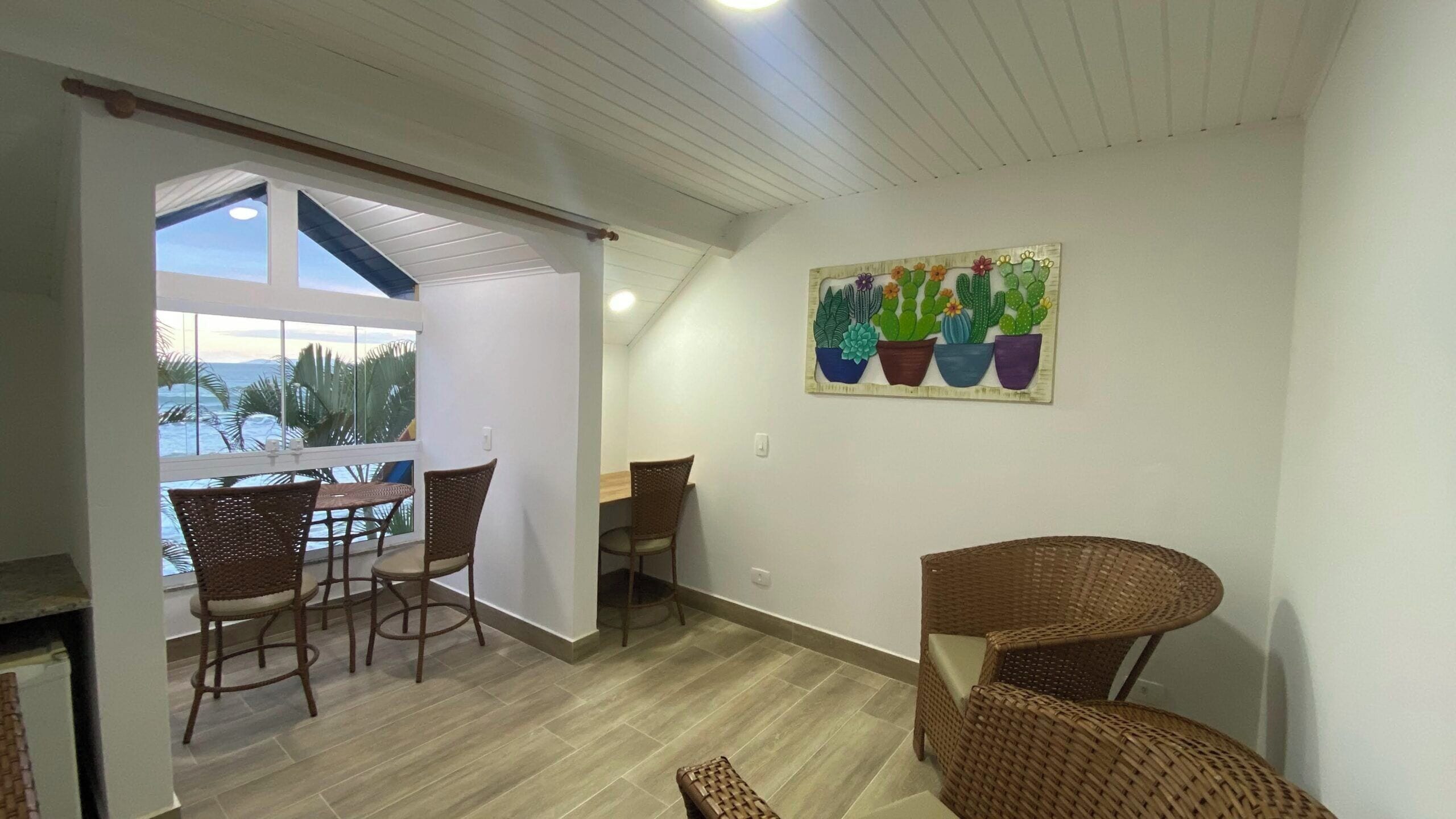 Ein Essbereich mit Korbstühlen und einem Tisch, ein Balkon mit Blick und Wandkunst mit Kaktusmotiven.