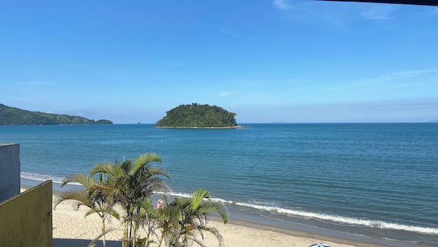 A beach with a sandy shore, palm trees, and a small island in the distance. - Pousada Kaliman Ubatuba (Ubatuba)