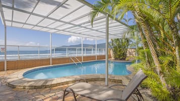 Piscina interior con vista al océano, rodeada de palmeras y una zona cubierta con techo de cristal.