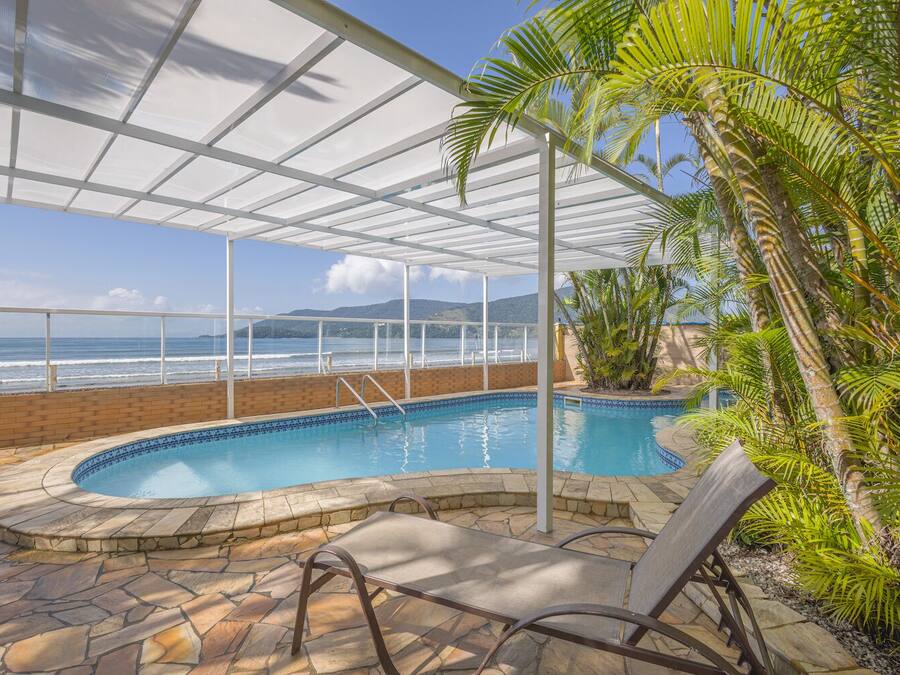 Piscina interior con vista al océano, rodeada de palmeras y una zona cubierta con techo de cristal.