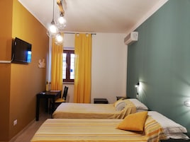 Habitación de hotel con dos camas, un escritorio, una silla, un televisor y una ventana con cortinas amarillas.