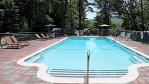 A rectangular swimming pool with a tiled deck, surrounded by lounge chairs and umbrellas. - Forest Hill Lodge & Cabins (Lake George)