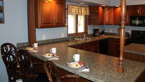 A kitchen with granite countertops, wooden cabinets, and a central island with breakfast items. - Forest Hill Lodge & Cabins (Lake George)