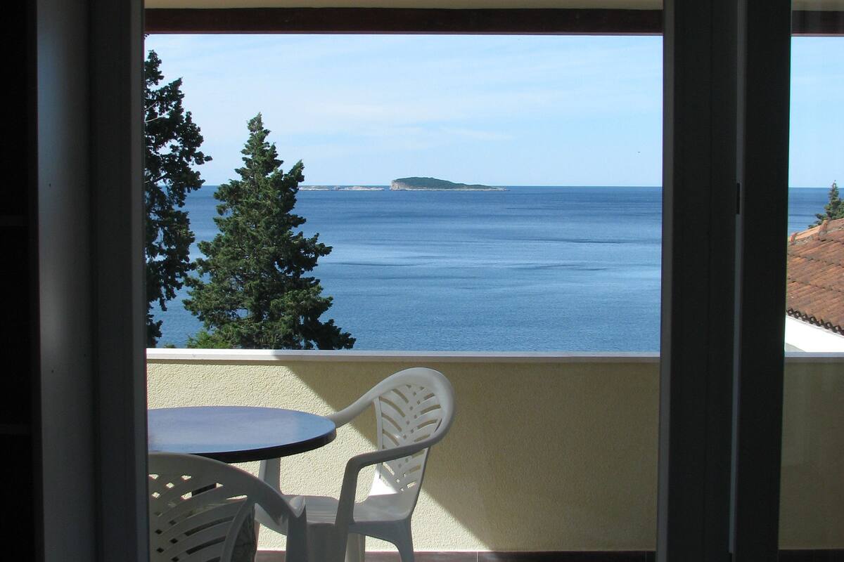 A balcony with a table and chairs, overlooking a body of water and a distant island.