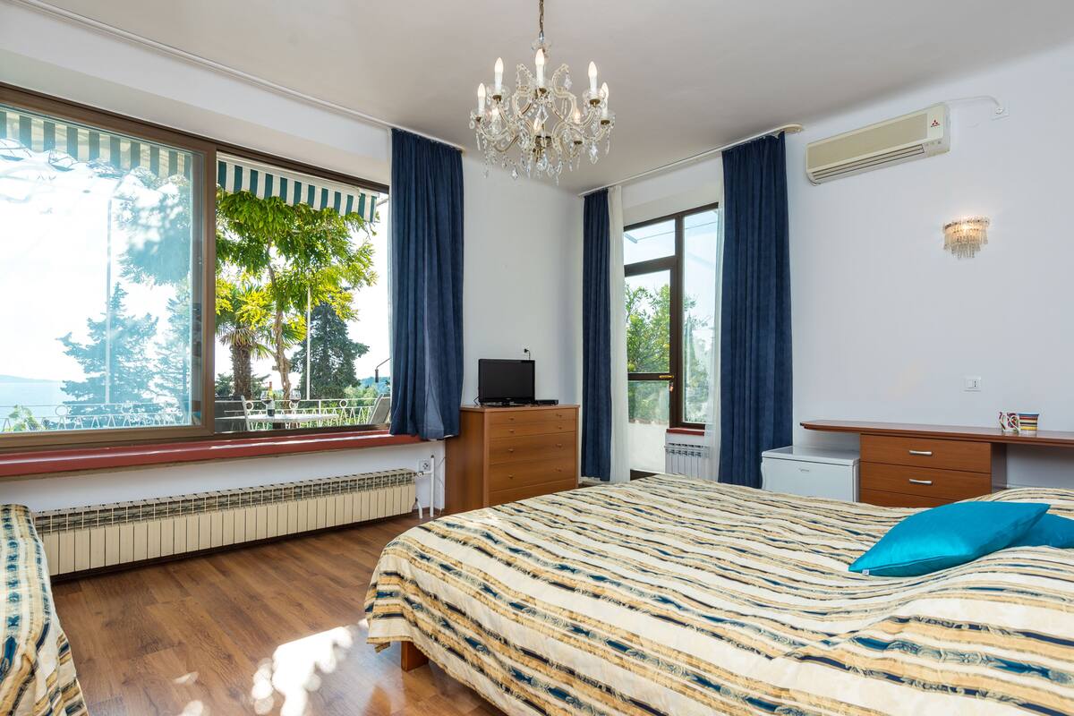 A bedroom with a large bed, a dresser, a television, and a window with curtains.