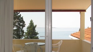 Een balkon met een tafel en stoelen, uitzicht op zee en een betegelde vloer.