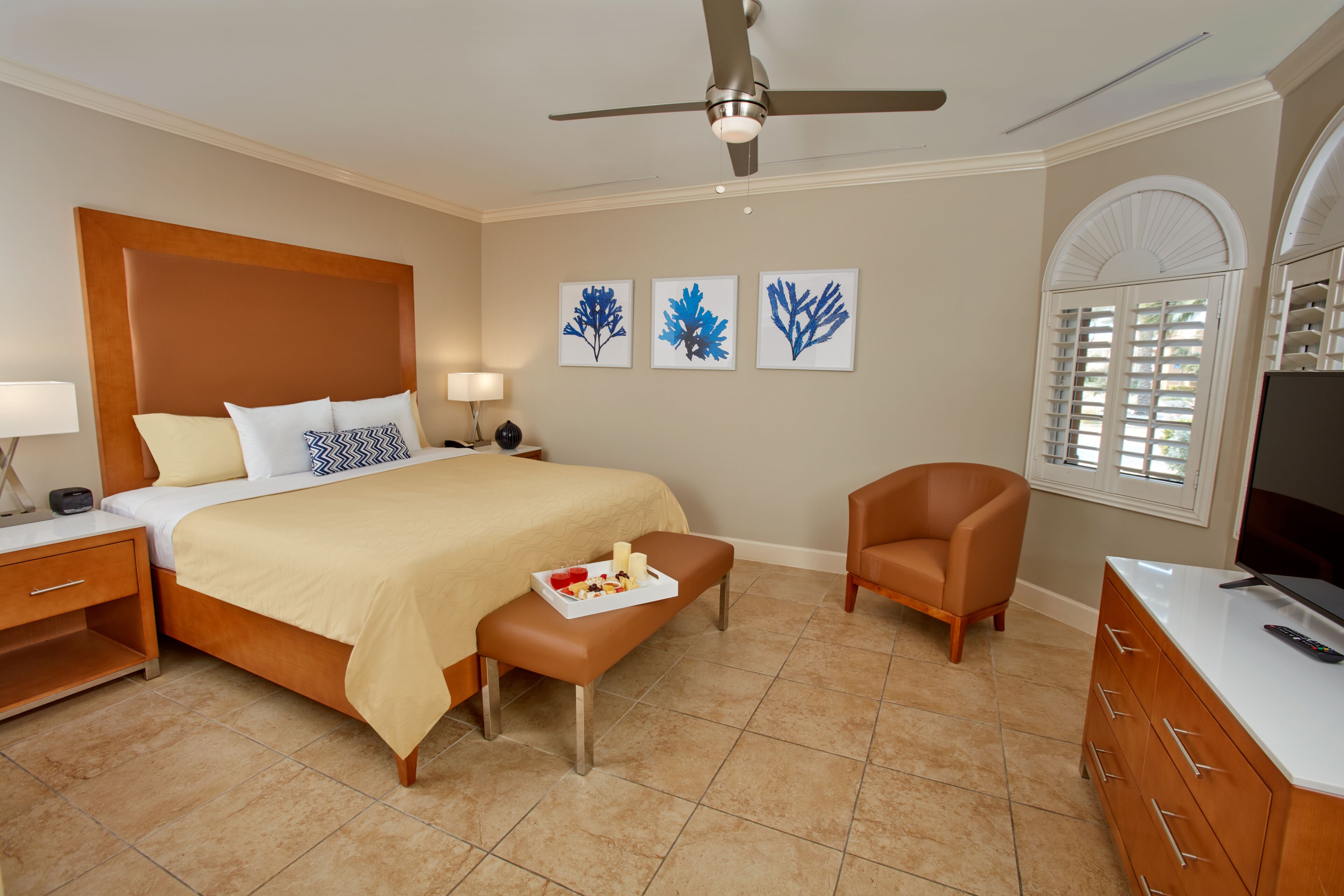 A hotel room with a bed, a chair, a TV, and artwork on the wall.