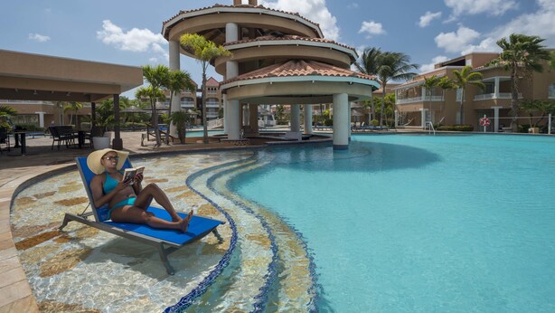 A pool area with a lounge chair, a gazebo, and a building with a tower.