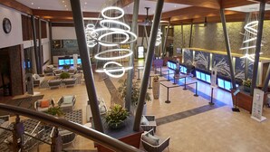 A spacious lobby with a modern design, featuring a central seating area with sofas and chairs, a reception desk, and a staircase with a glass railing.