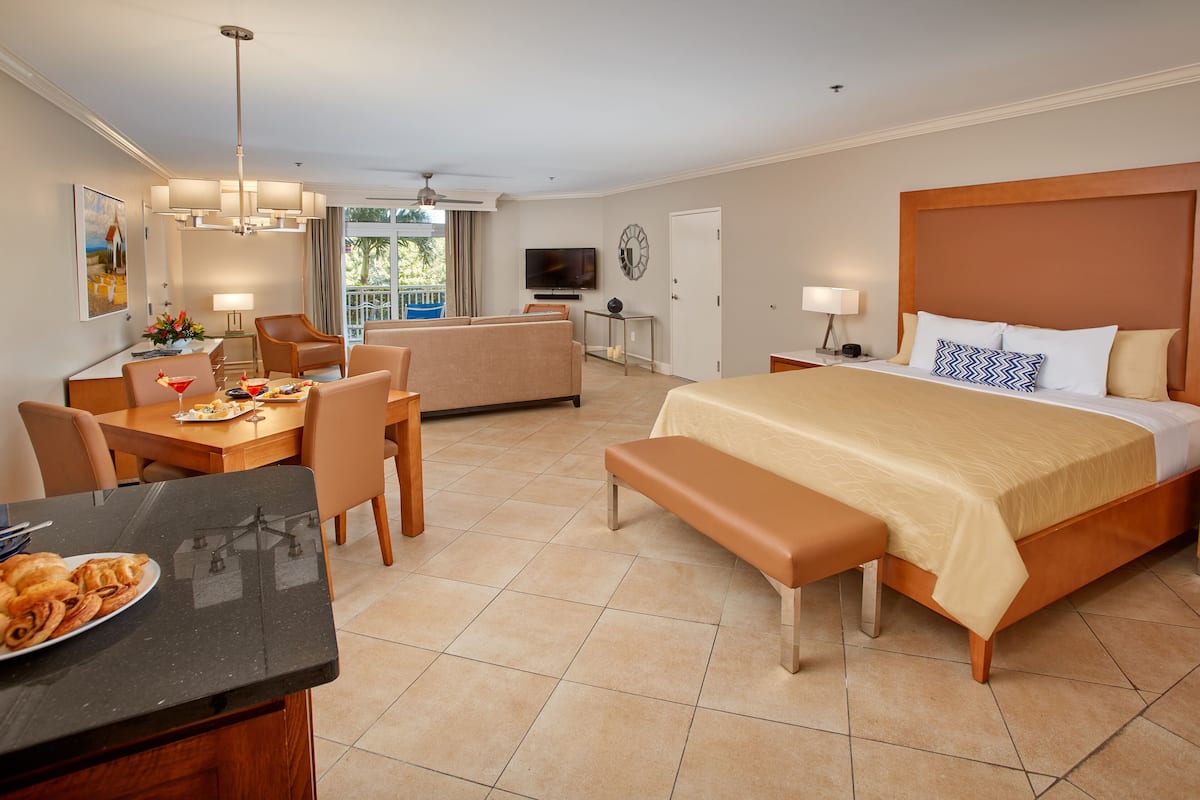 A hotel room with a bed, a desk with a chair, a sofa, and a dining area with a table and chairs.