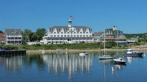Un hôtel situé au bord de l’eau, avec plusieurs étages, un drapeau au sommet et plusieurs bateaux amarrés sur le port.