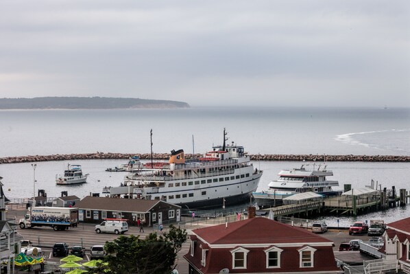Uma cidade costeira com um grande ferry atracado no cais, rodeada por edifícios e uma linha costeira rochosa.