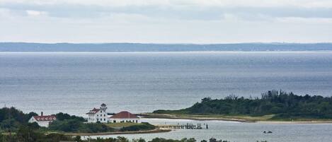 A coastal view with a white building with a red roof, a pier extending into the water, and a distant shoreline.