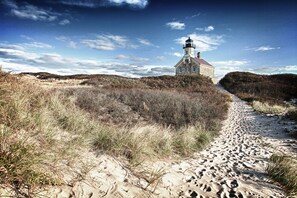 Un phare se dresse sur un sentier sablonneux, entouré de végétation.
