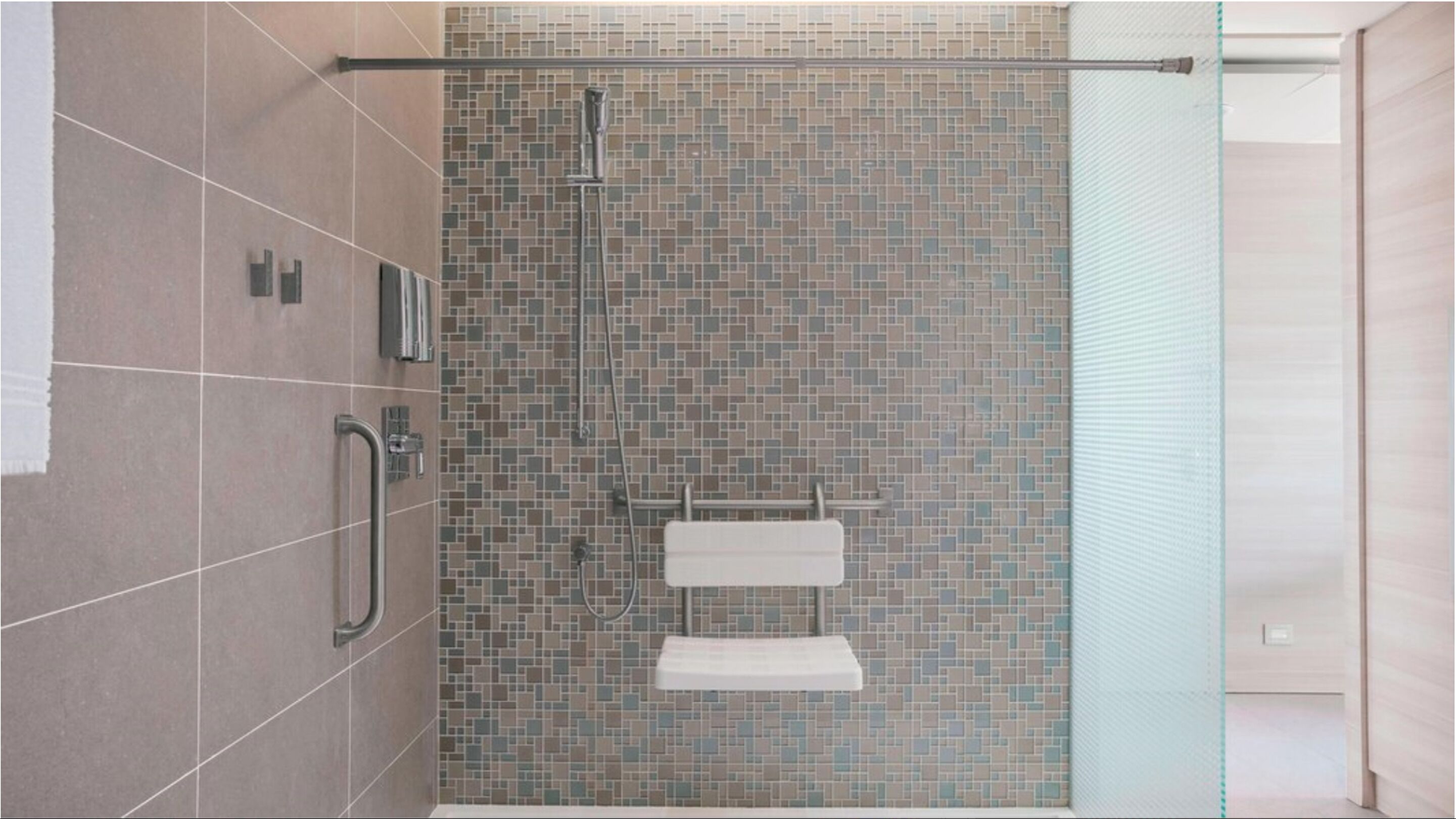 A modern shower with a tiled mosaic wall, a glass door, and a towel rack.