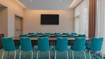 Un salón de conferencias con sillas color turquesa, una mesa larga y una pantalla grande en la pared.