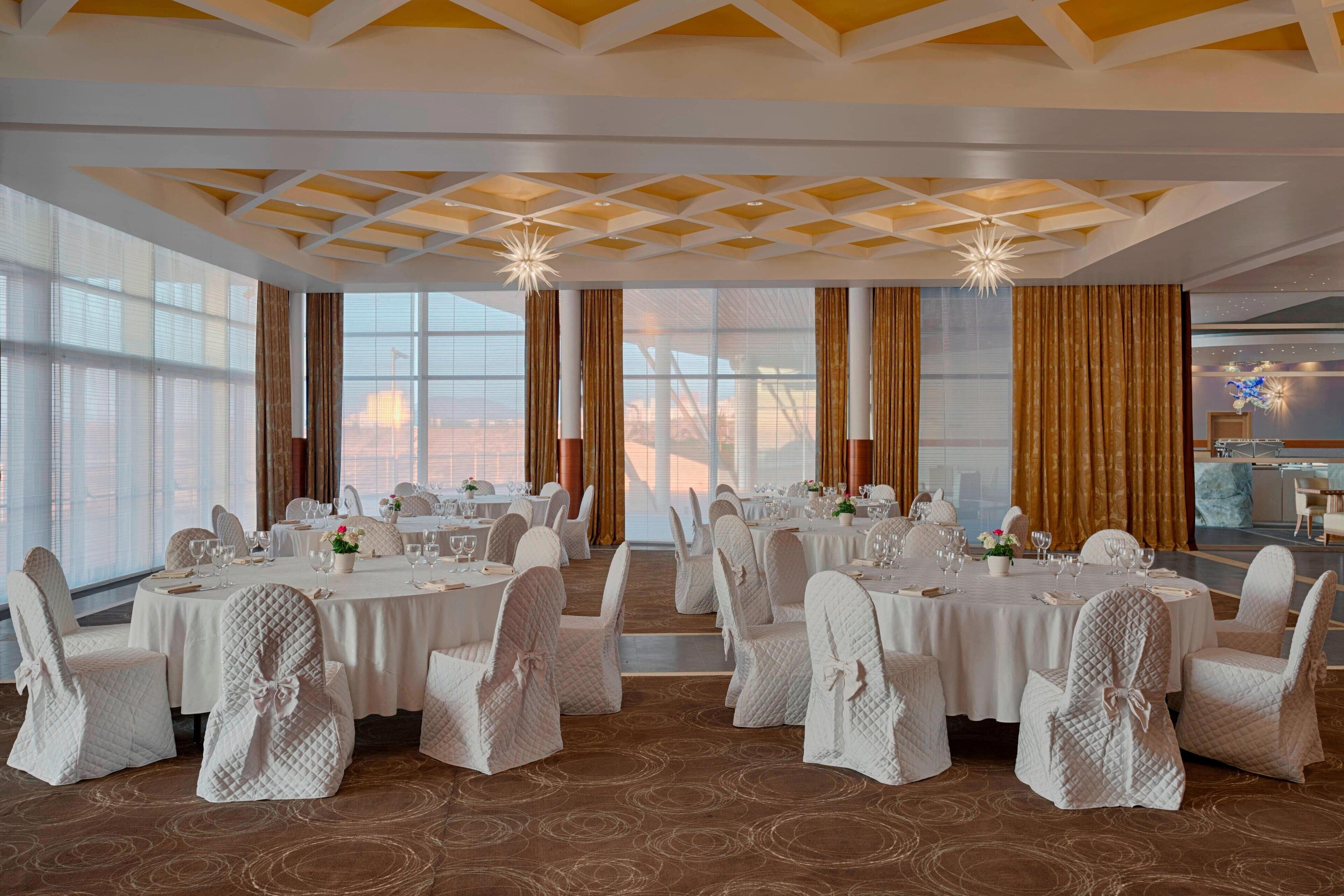 A banquet hall with round tables, white tablecloths, and chairs with white covers.
