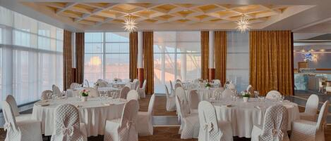 A banquet hall with round tables, white tablecloths, and chairs with white covers.