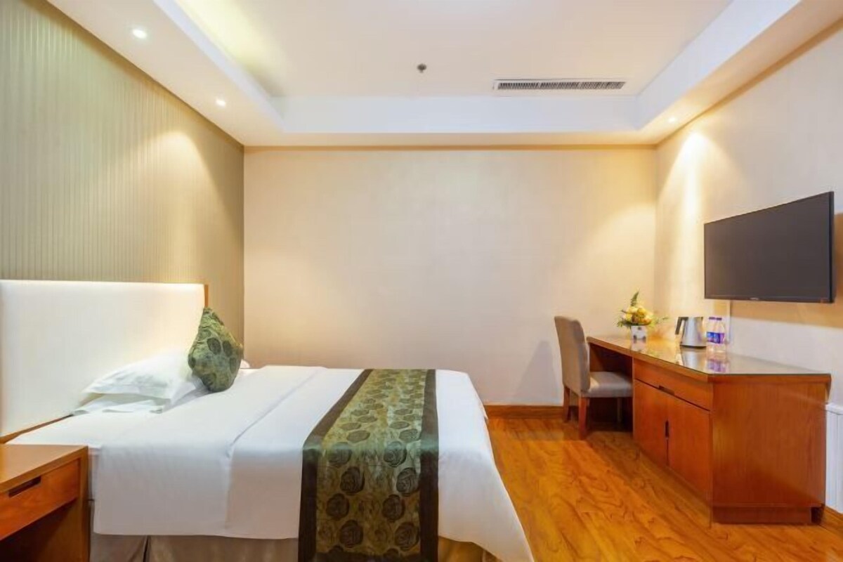 A hotel room with a bed, a desk, a chair, a TV, and a wooden cabinet.