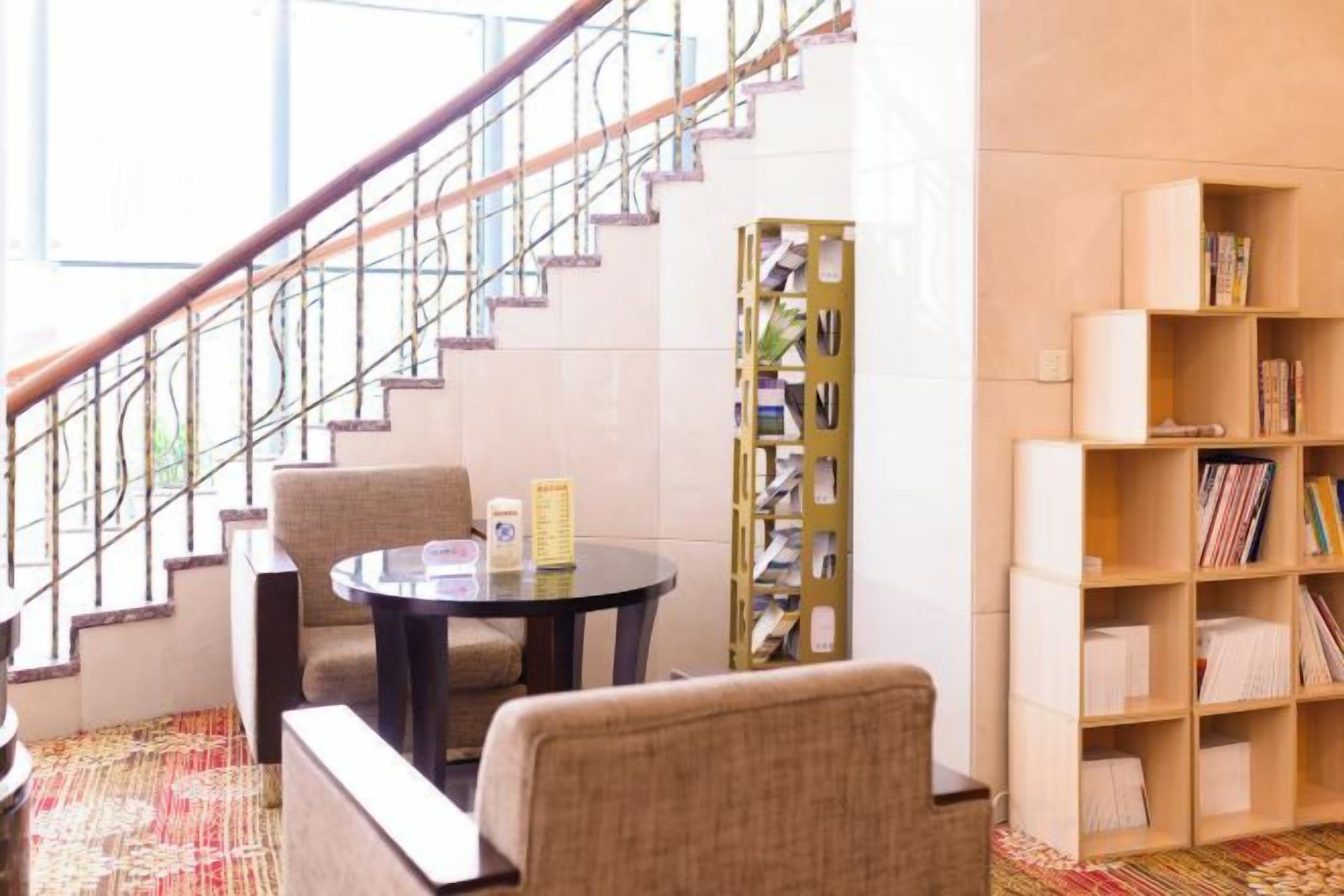 Una escalera con barandilla, una mesa redonda con sillas y una estantería con libros.