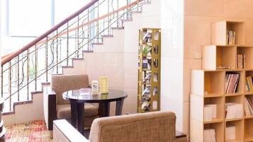 Una escalera con barandilla, una mesa redonda con sillas y una estantería con libros.