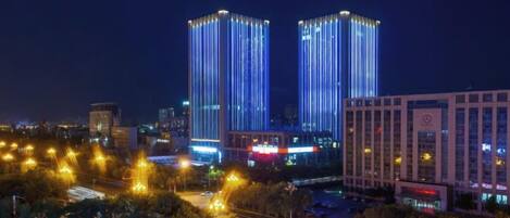 Un paisaje urbano nocturno con edificios iluminados y un área de estacionamiento.