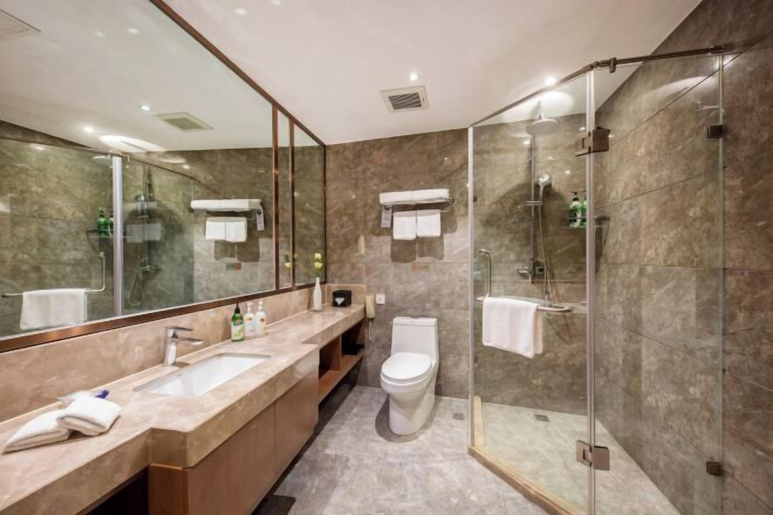 A modern bathroom with a glass-enclosed shower, a large mirror, and a marble countertop.