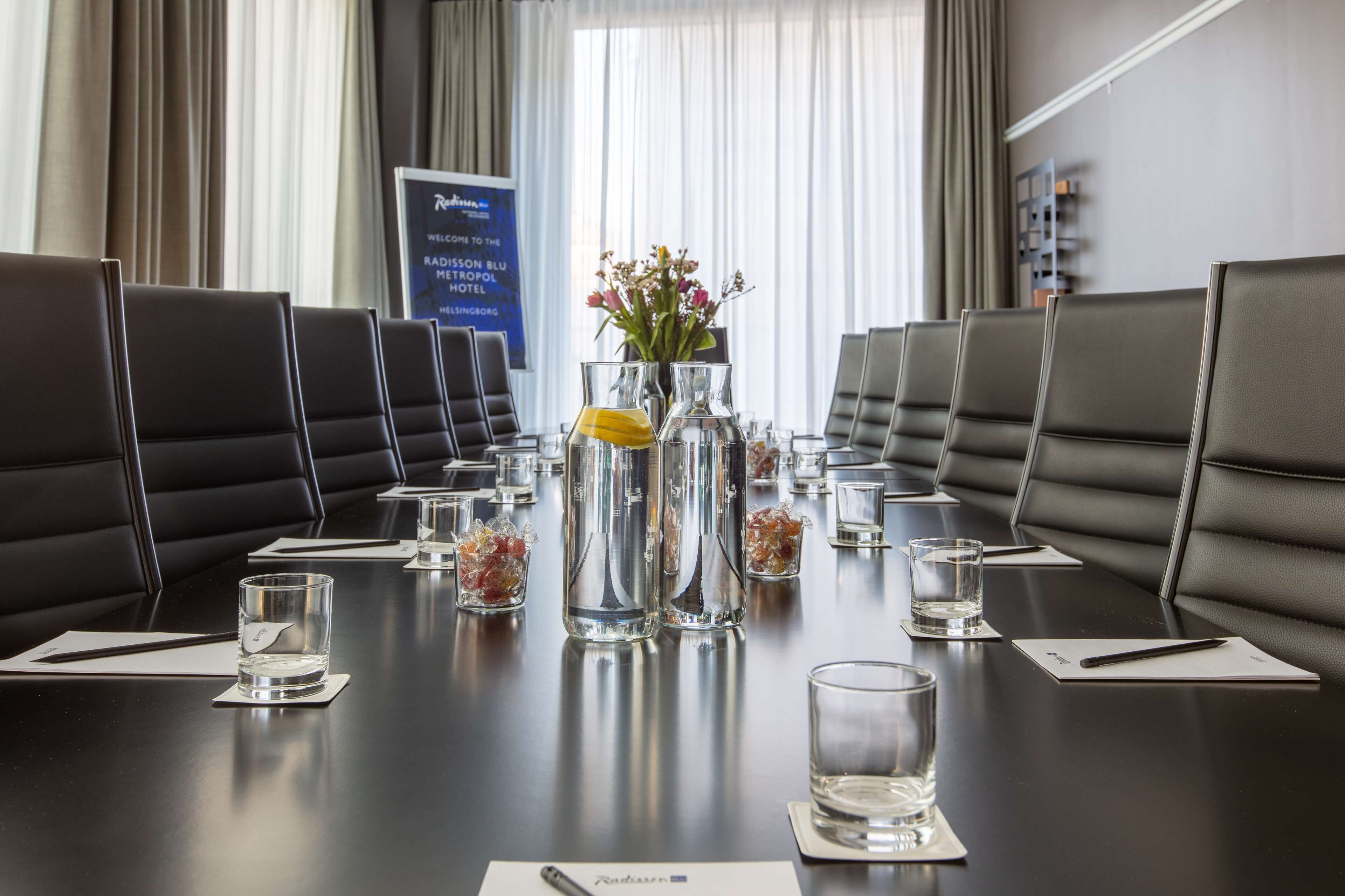 A conference room with a long table, black leather chairs, and a vase with flowers.