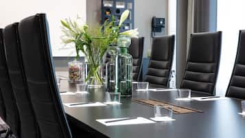 Un salón de conferencias con una larga mesa, sillas de cuero negro y un jarrón con flores.