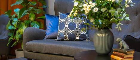 A grey sofa with a patterned pillow, a vase with flowers, and a stack of books on a small table.
