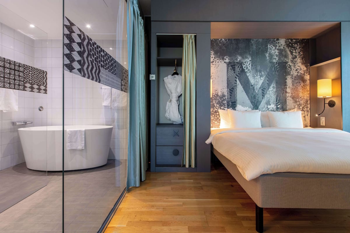 A modern hotel room with a large bed, a bathtub, and a walk-in closet.