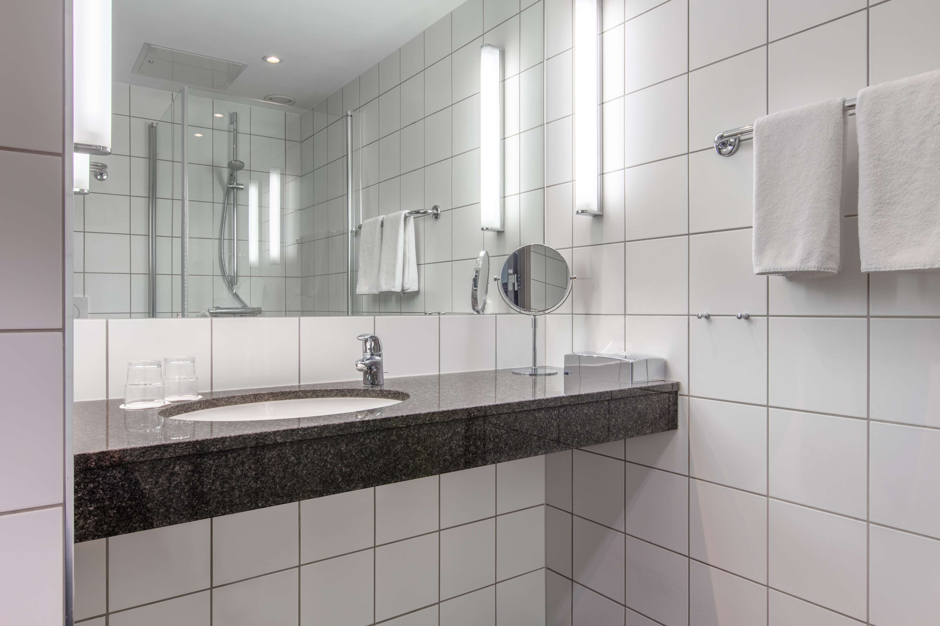 A modern bathroom with a granite countertop, a sink, a mirror, and a towel rack.
