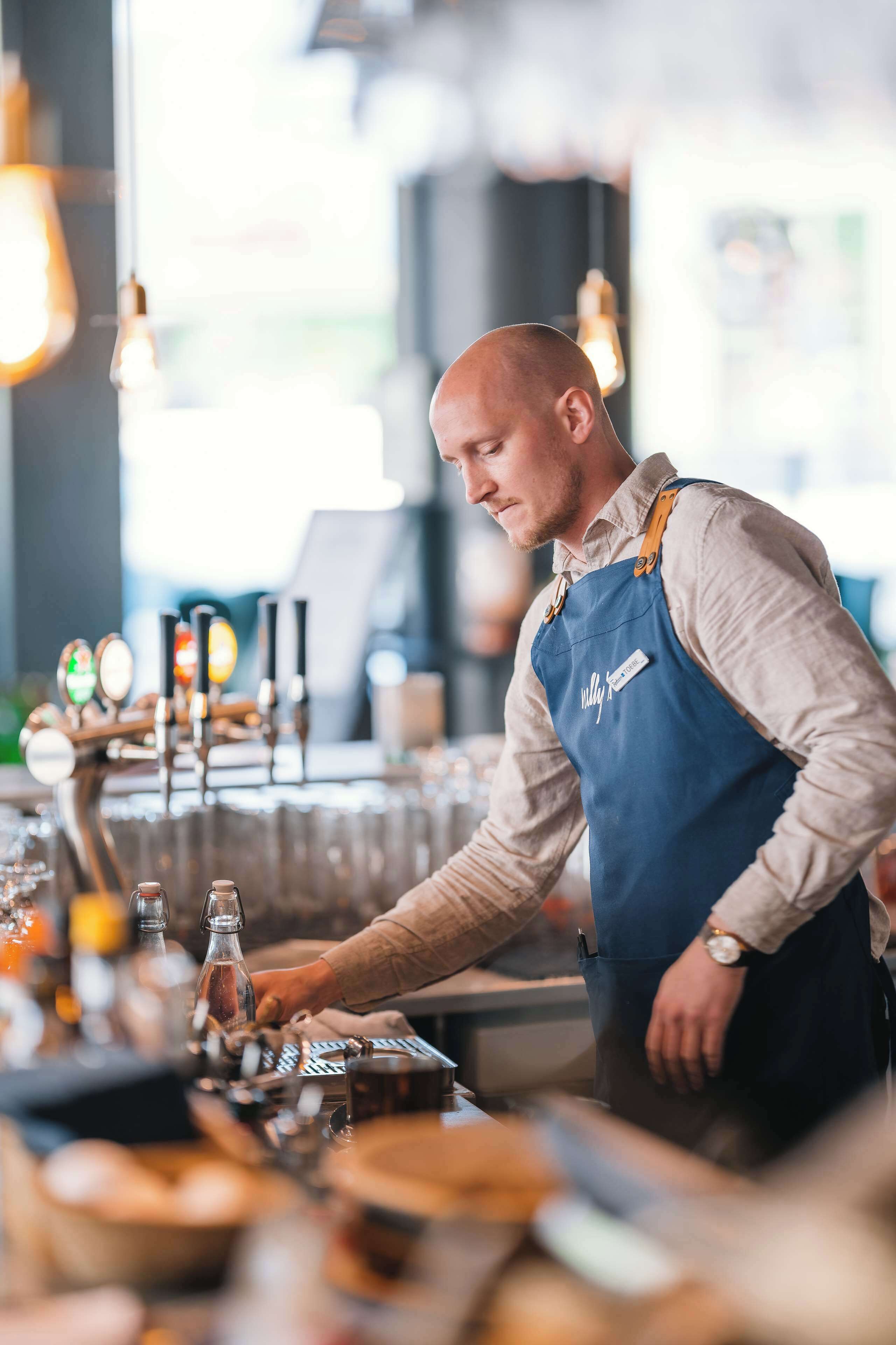A barista preparing a drink at a counter with a coffee machine and various bar tools.