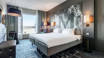 A hotel room with a large bed, two bedside tables, a desk, a chair, and a view of the city.