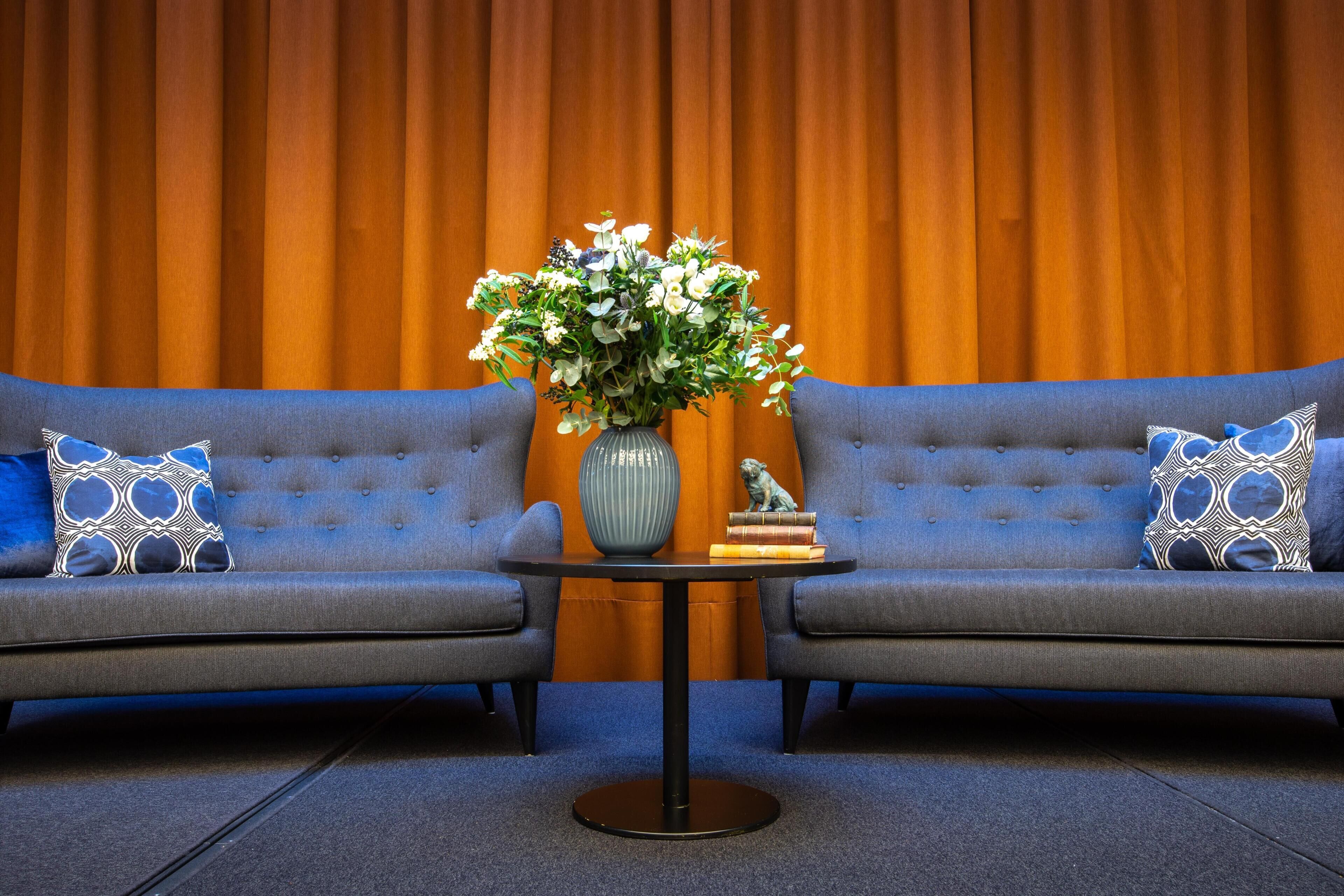 A room with two grey sofas, a small round table with a vase of flowers, and a statue on the table.