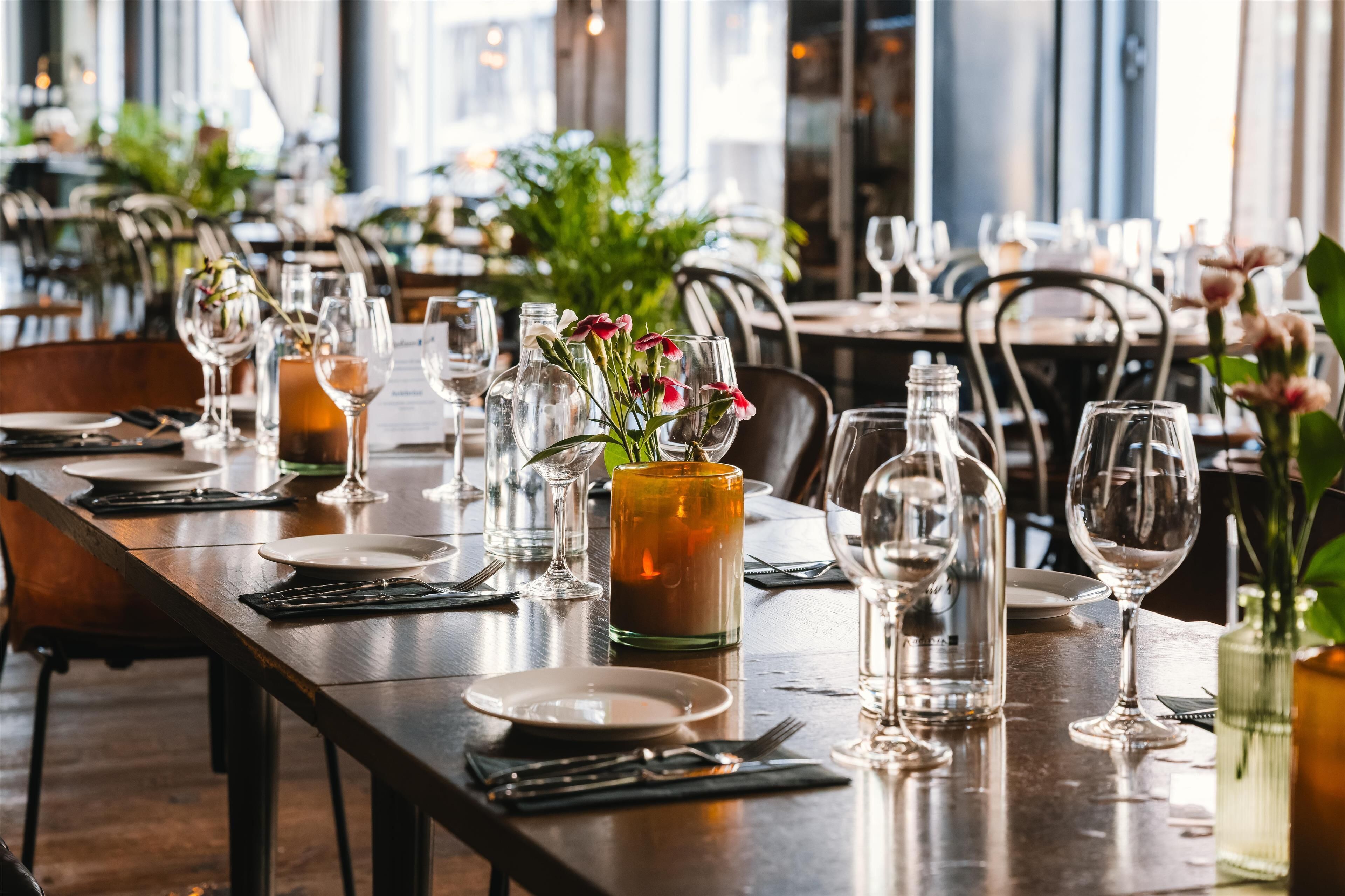 A restaurant with long wooden tables set for dining, clear glassware, and small vases with flowers.