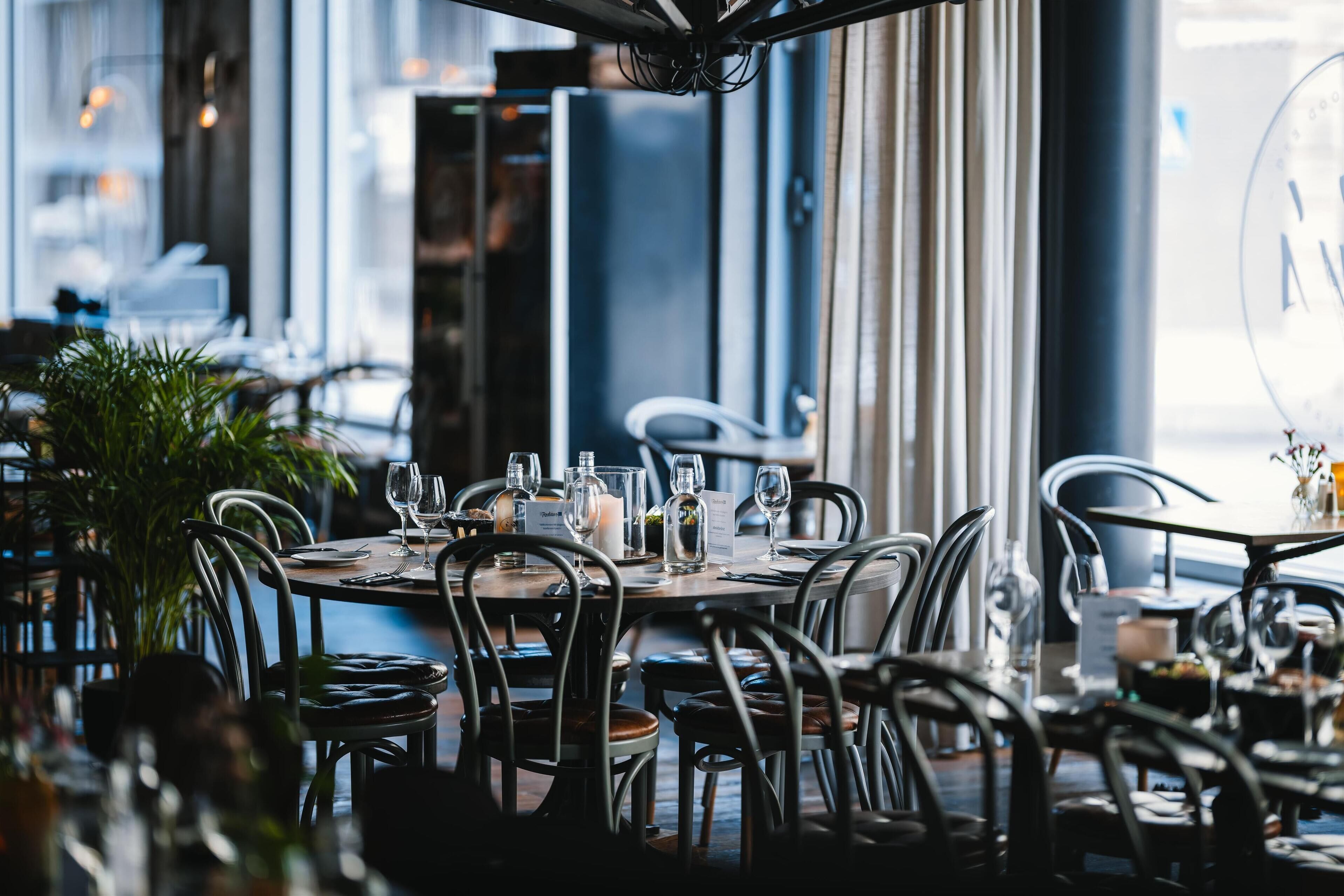 Un restaurante con mesas redondas, sillas de metal y plantas en macetas.