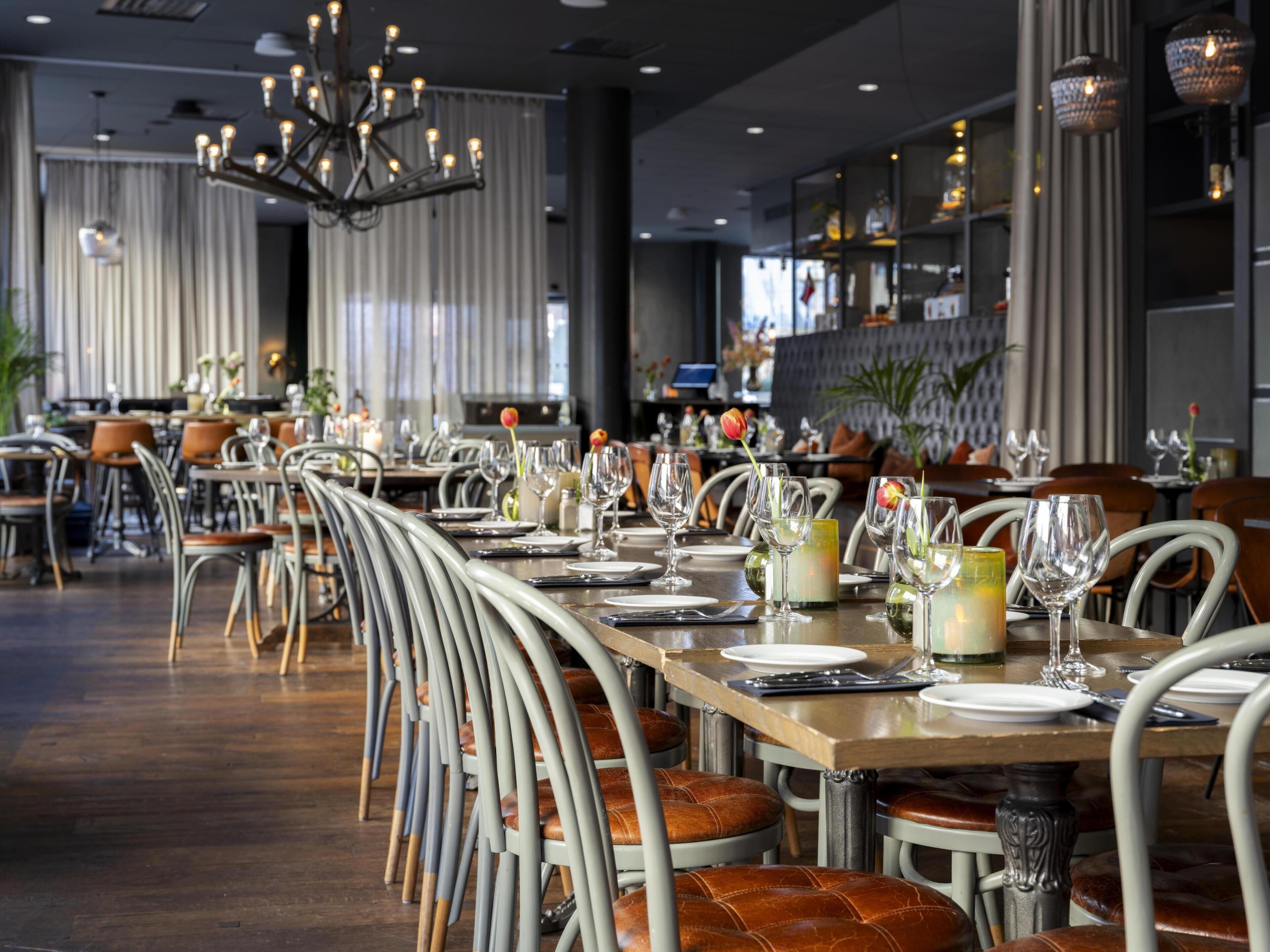 Een restaurant met lange tafels, stoelen en een kroonluchter.