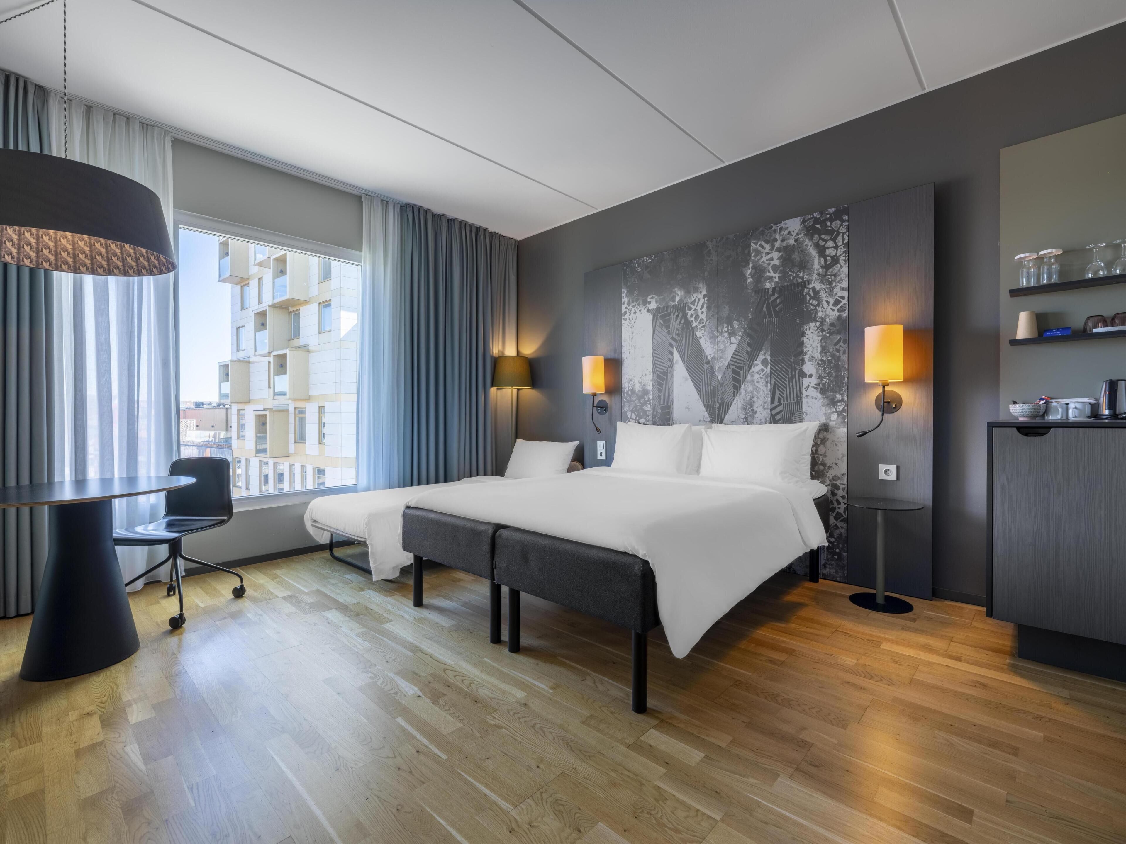 Une chambre d’hôtel moderne avec un grand lit, deux tables de chevet, un bureau et une chaise.